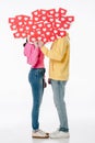 Couple in blue jeans and hoodies hiding faces behind red paper cut cards with hearts symbols on white background Royalty Free Stock Photo