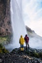 Couple in bright clothes looks at an Icelandic waterfall