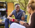 Couple Camping In Countryside With RV Sitting In Chairs Drinking Coffee By Outdoor Fire Royalty Free Stock Photo