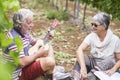 Couple of caucasian adult senior stay together outdoor in leisure activity playing an ukulele guitar doing serenade for the lady.