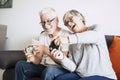 Couple of caucasian retired seniors playing videogames together at home sitting on the sofa - mature woman and man married - two Royalty Free Stock Photo