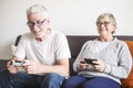 Couple of caucasian retired seniors playing videogames together at home sitting on the sofa - mature woman and man married - two Royalty Free Stock Photo