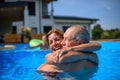 Couple of cheerful seniors shaving fun in pool with friends jumping, swiming and lounging on floats. Elderly friends Royalty Free Stock Photo