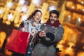 Couple in the city centre with holiday`s brights in background. Couple browsing digital tablet. They are using credit card Royalty Free Stock Photo