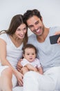 Couple clicking selfie with baby on bed Royalty Free Stock Photo