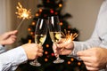 Couple clinking glasses with champagne and holding sparklers on background of christmas tree, celebrating christmas at home Royalty Free Stock Photo