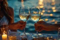 A couple clinking white wine glasses at sunset, overlooking the sea