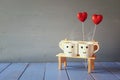 Couple coffee cups on old bench next to red hearts