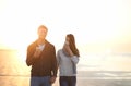 Couple, coffee and walk at beach on vacation, sunset and holding hands in portrait by ocean. Man, woman and drink with Royalty Free Stock Photo