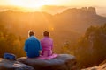 Couple in colorful jackets enjoying sunset atop the viewpoint in the mountains.