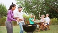 Couple cooking on a barbaque in countryside. At the back, his friends celebrating with alcohol drinks.