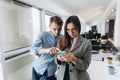 Couple of coworkers, students sharing together smartphone, standing in creative office