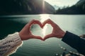 couple creating heartshape with joined hands over lake