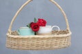 Couple cups of tea or coffee and two red roses hanging in a wooden rattan basket on blue background. Still life concept. Royalty Free Stock Photo