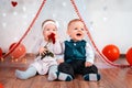 A couple of cute babies posing on a white background decorated with hearts. A happy girl eating a rose in her hands. Valentine`s