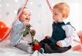 A couple of cute babies posing on a white background decorated with hearts. A happy girl holds a rose in her hands. Valentine`s