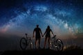 Couple cyclists with mountain bikes at night under starry sky