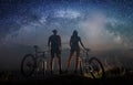 Couple cyclists with mountain bikes at night under starry sky