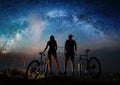 Couple cyclists with mountain bikes at night under starry sky