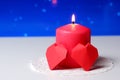 Couple of 3D red paper hearts, burning pink candle on white openwork paper napkin, blue bokeh snow background closeup view Royalty Free Stock Photo