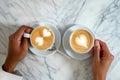 Couple on a date, man and woman hands holding coffee cup with latte art. Cappuccino crema of heart shape. Top view of marble cafe Royalty Free Stock Photo