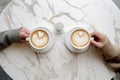 Couple on a date, two people, hands holding coffee cup with latte art. Cappuccino crema of heart shape. Top view of marble cafe Royalty Free Stock Photo