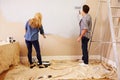 Couple Decorating Room Using Paint Rollers On Wall