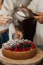 Couple decorating together a homemade cheesecake with fresh berries and icing sugar Royalty Free Stock Photo