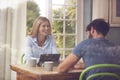 Couple With Digital Tablet Sitting At Table Working From Home Viewd Through Window