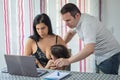 Couple works and watches laptop computer at home while baby takes mother`s breast Royalty Free Stock Photo