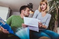 Couple doing accounting on line with a phone bank app sitting on a couch in the living room