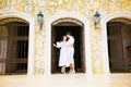 Couple dressed in white, stands in arch of house