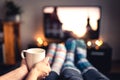 Couple drinking tea, hot chocolate, eggnog or mulled wine and watching tv in warm cozy woolen socks in winter.