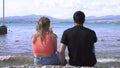 Couple drinking wine on stone beach. Media. Young man and woman drink wine sitting on rocky shore near blue sea. Young