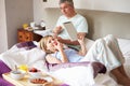 Couple Eating Breakfast In Bed With Paper And Digital Tablet