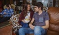 Couple eating chips on a sofa and friend looking Royalty Free Stock Photo