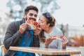 Couple eating pizza outdoors and smiling.