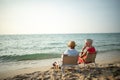 A couple of elderly sitting in chairs at the beach watching the sun and the sea on their summer vacation and they smile and enjoy Royalty Free Stock Photo