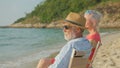 A couple of elderly sitting in chairs at the beach watching the sun and the sea on their summer vacation and they smile and enjoy Royalty Free Stock Photo