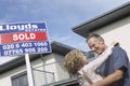 Couple Embracing By Sold Sign Outside New Home