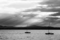 A couple of empty, little sailboat on a lake, beneath a moody sky with sun rays filtering through.