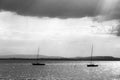 A couple of empty, little sailboat on a lake, beneath a moody sky with sun rays filtering through.