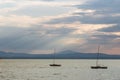 A couple of empty, little sailboat on a lake, beneath a moody sky with sun rays filtering through