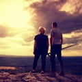 Couple enjoying marvellous moments during sunset . Young pair of hikers on the peak of rock watch over valley to Sun.