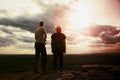 Couple enjoying marvellous moments during sunset . Young pair of hikers on the peak of rock watch over valley to Sun. Royalty Free Stock Photo