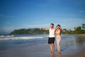 Couple enjoys beach stroll, man pointing horizon, woman smiles, tropical island escape. Ocean sand, vacation vibes Royalty Free Stock Photo