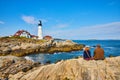 Couple enjoys view of lighthouse on Maine coastline sitting on rocks