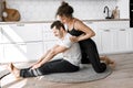 Couple exercising together on the modern kitchen floor. Man and woman in sports wear doing workout at home. Caring girl