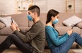 Couple in masks using smart phones sitting on floor Royalty Free Stock Photo