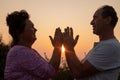 Couple facing each other against sunset, folding palms together and joining hands. Woman happily looking at man. Royalty Free Stock Photo